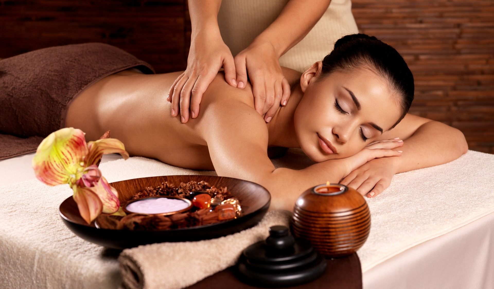 Woman receiving a back massage in a spa setting. Her eyes are closed, and a masseuse's hands are on her shoulders.