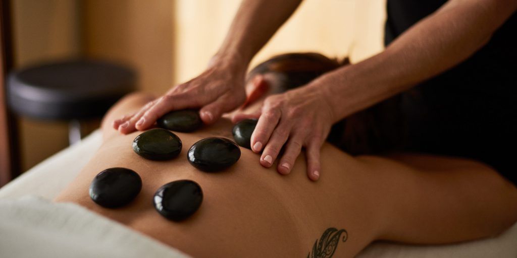 A person receiving a hot stone massage on their back. Dark stones are placed on the back by a massage therapist's hands.