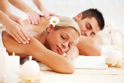 Couple receiving massages on their backs, lying face down in a spa setting, with candles lit around them.