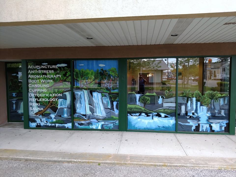 A business storefront with a painted mural of waterfalls and trees. Green trim surrounds the windows. Text on the left advertises acupuncture services.