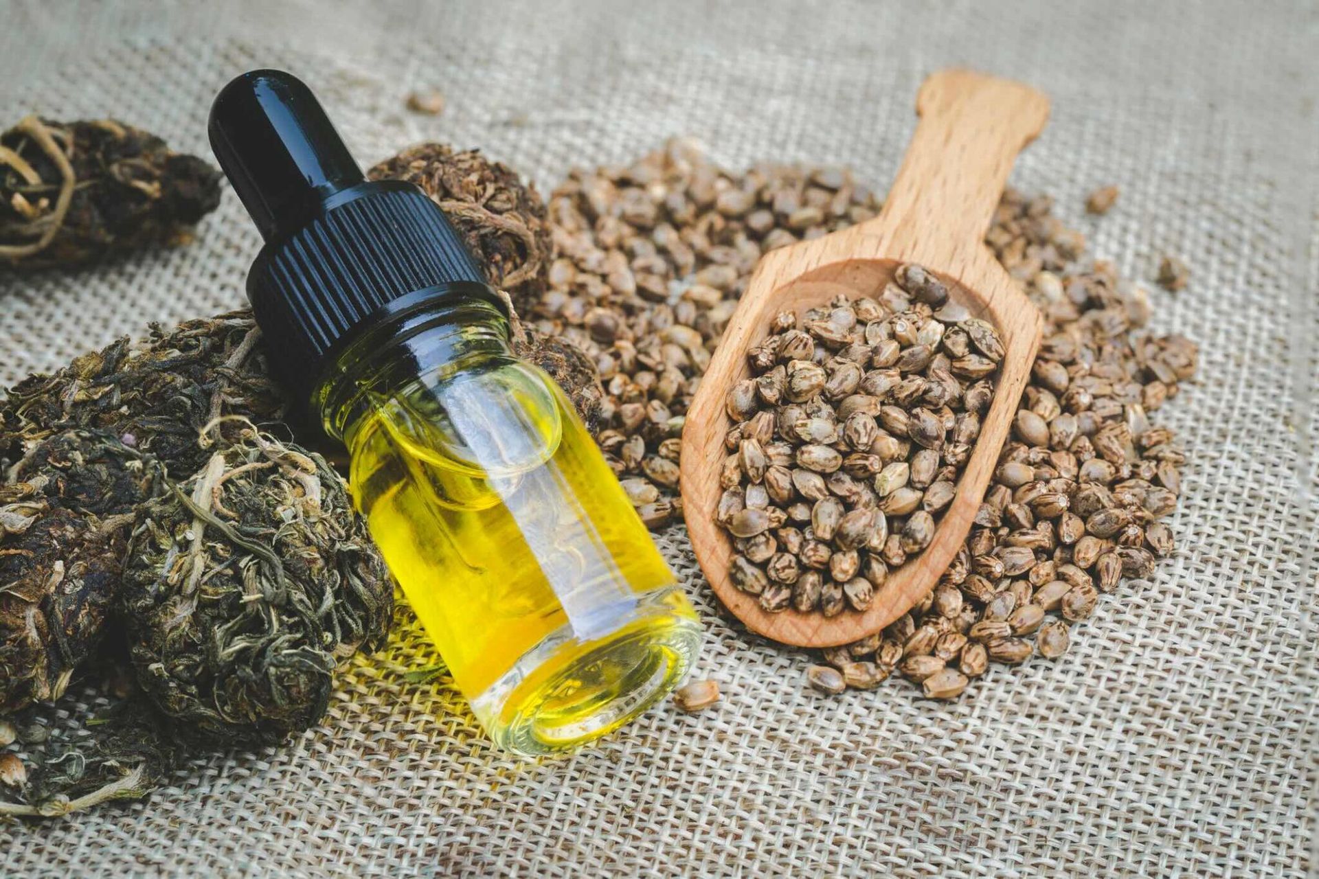 A bottle of oil next to a wooden spoon filled with hemp seeds.