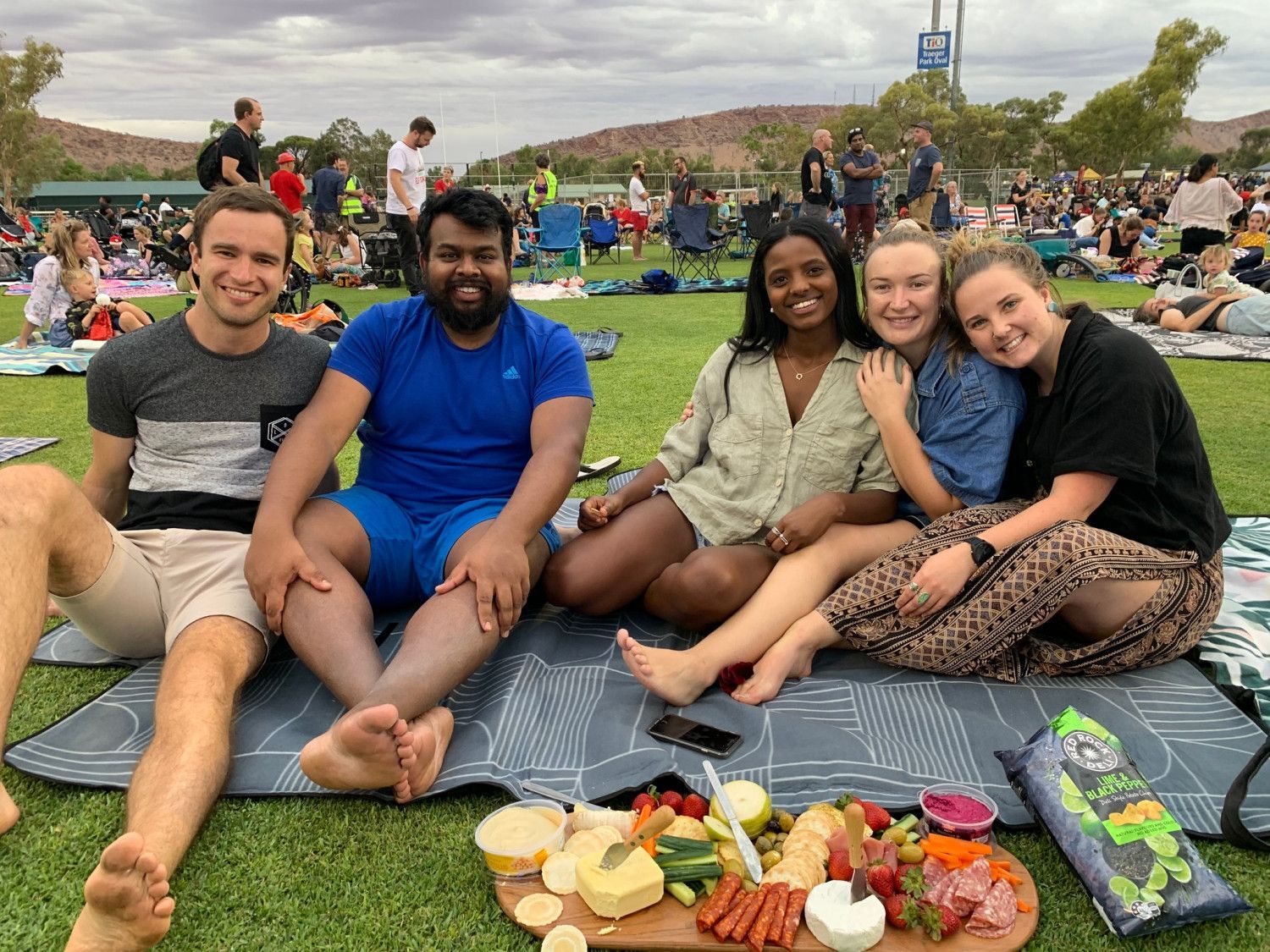 Group of friends enjoying picnic with food and drinks on the grass.