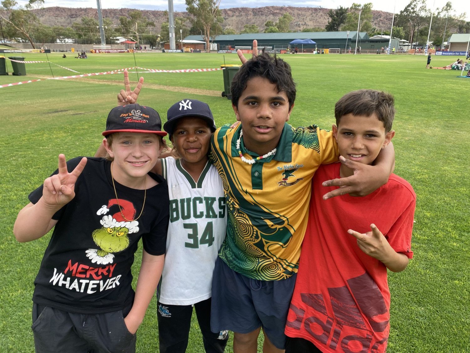 Four smiling children pose outside, making peace and other hand signs.