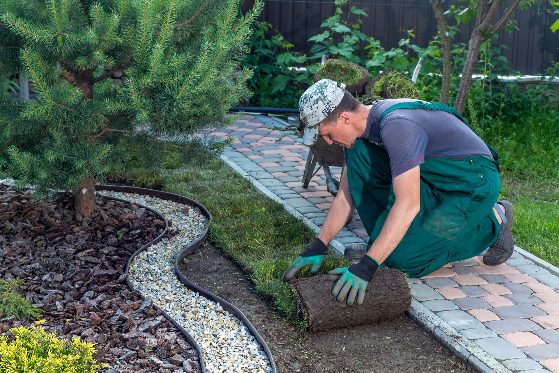 A male gardener with green uniform is performing landscape installation.