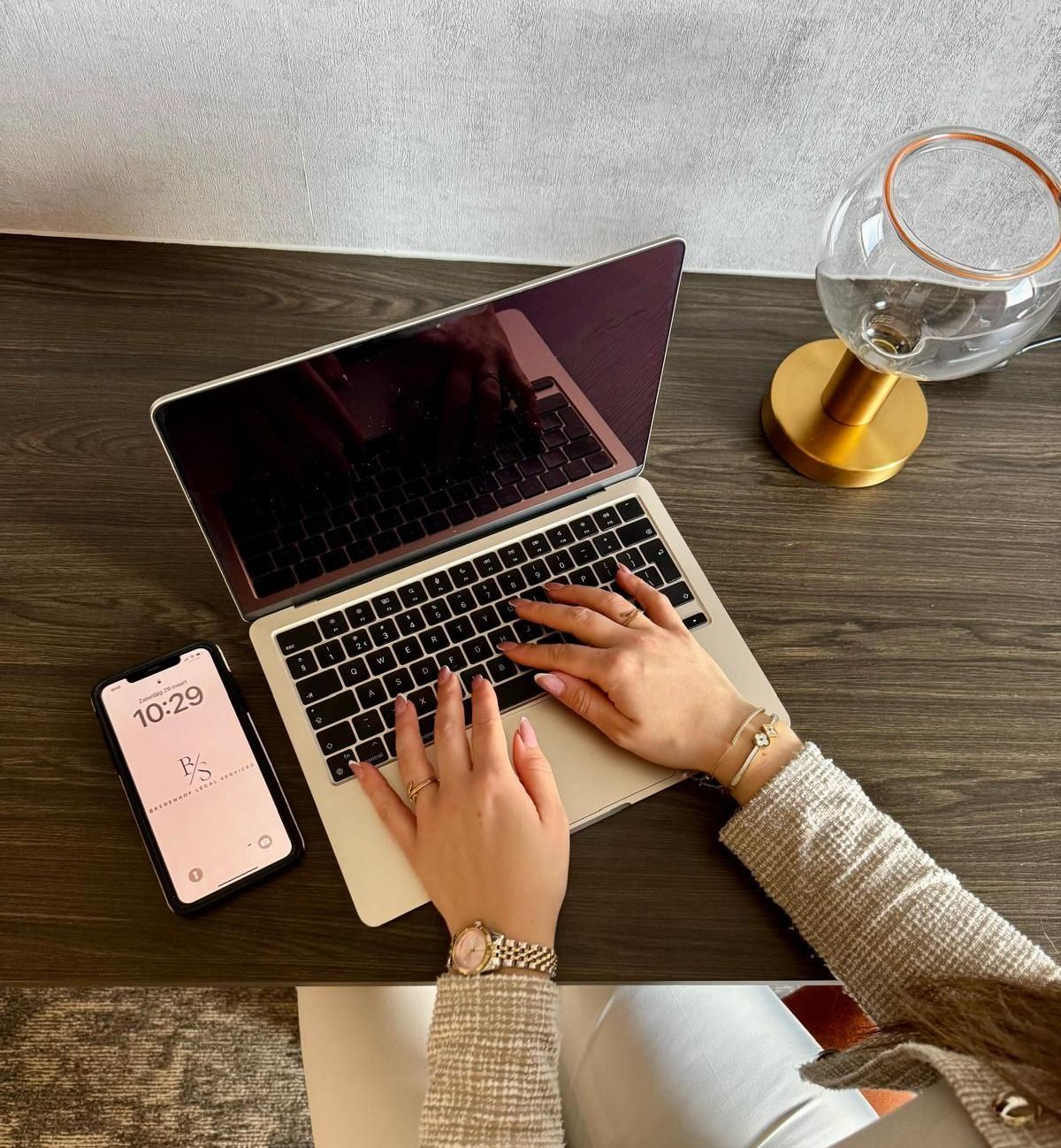 Een vrouw typt op een laptop met een telefoon naast zich