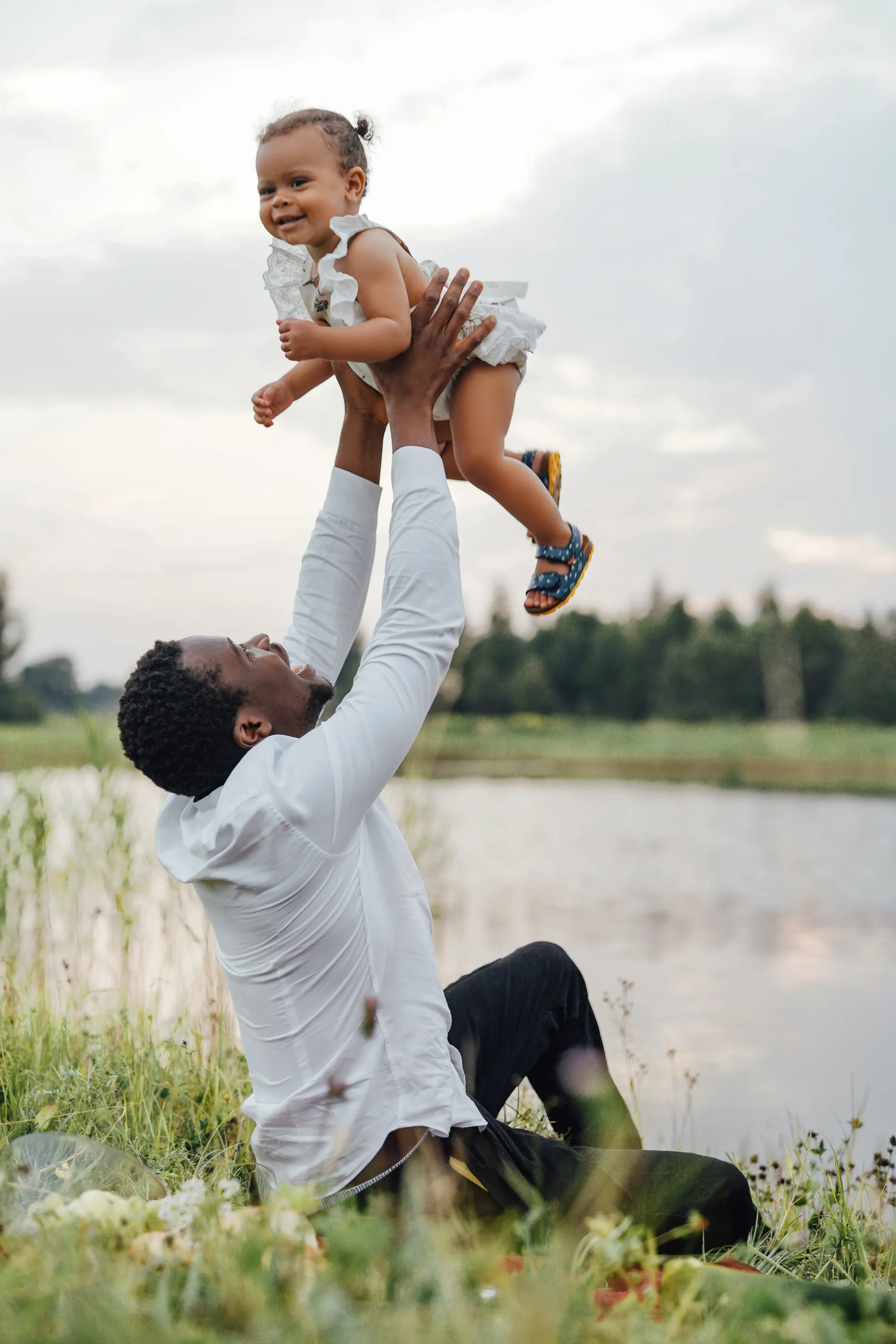 Man lifting child in the air near a lake; both smiling.