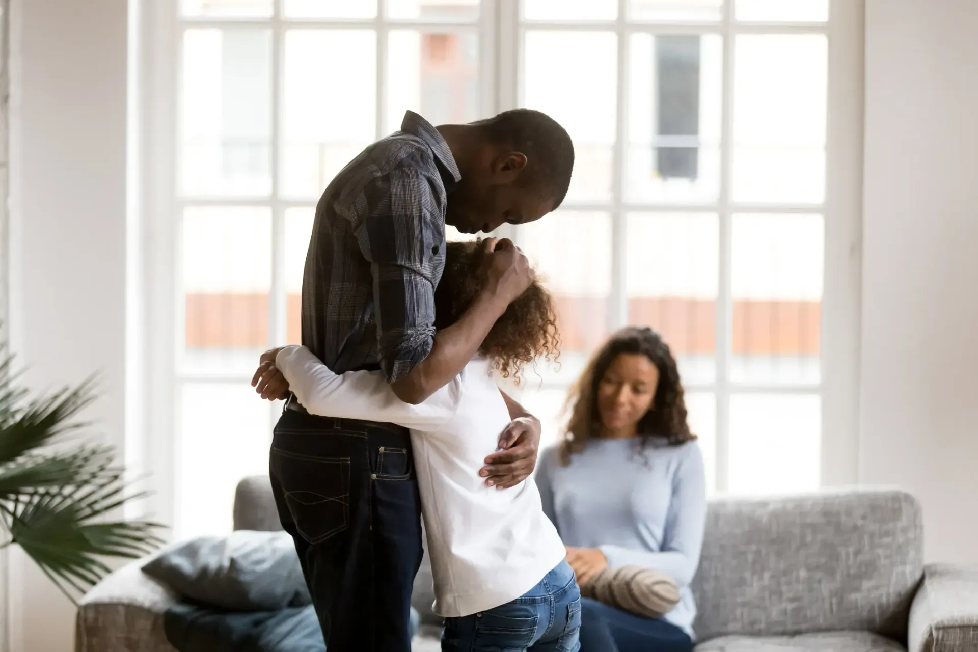 Family of four smiling, outdoors; mother holding child, father carrying child on his back.