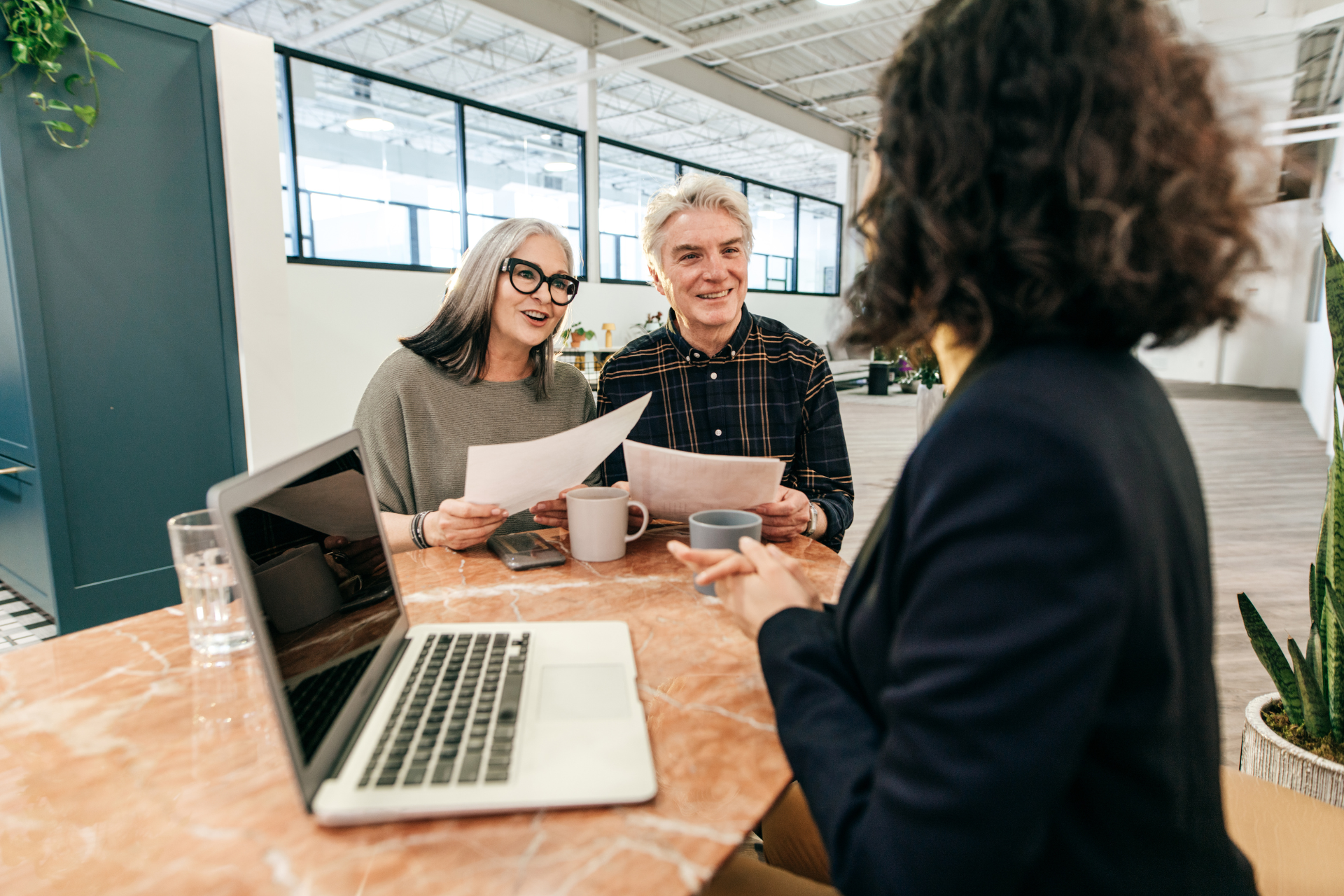 A woman is talking to a man and woman while sitting at a table with a laptop.