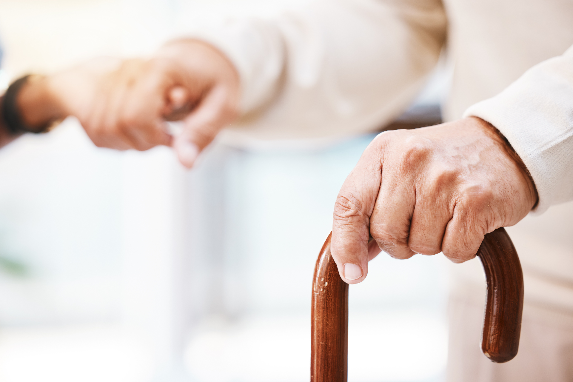 An elderly man is holding a wooden cane in his hand.