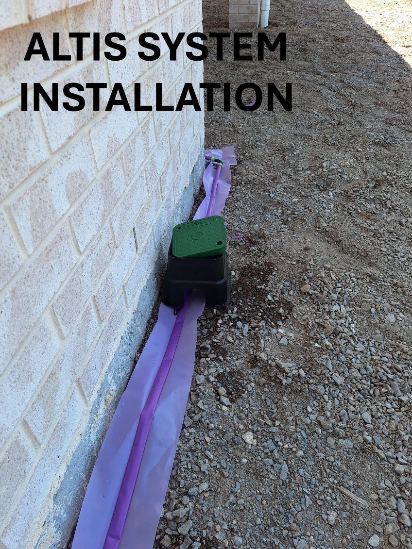 A purple drainage system installed near a brick wall; black box in the center, gravel ground.