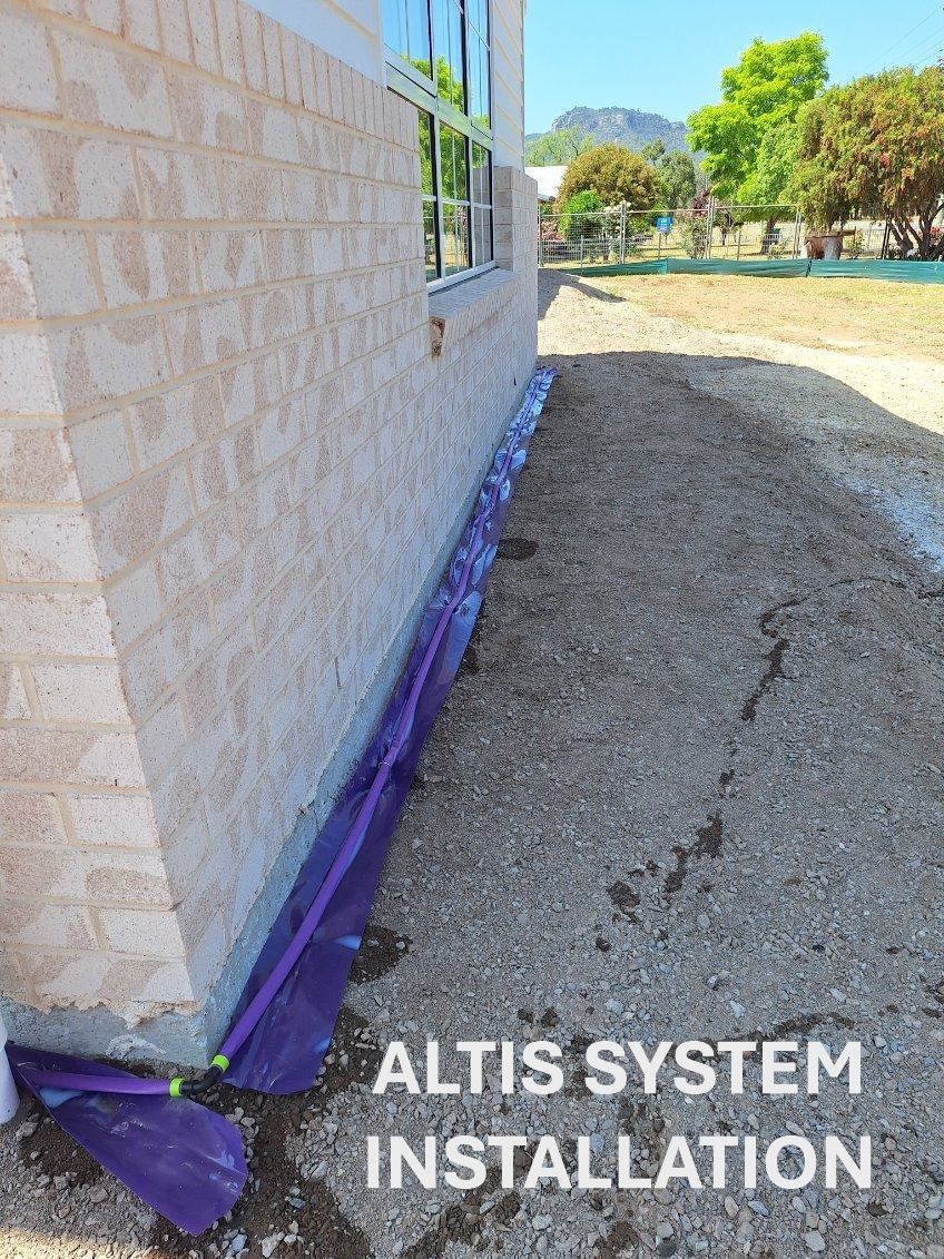 Purple ALTIS system installed at base of building's brick wall along gravel pathway.