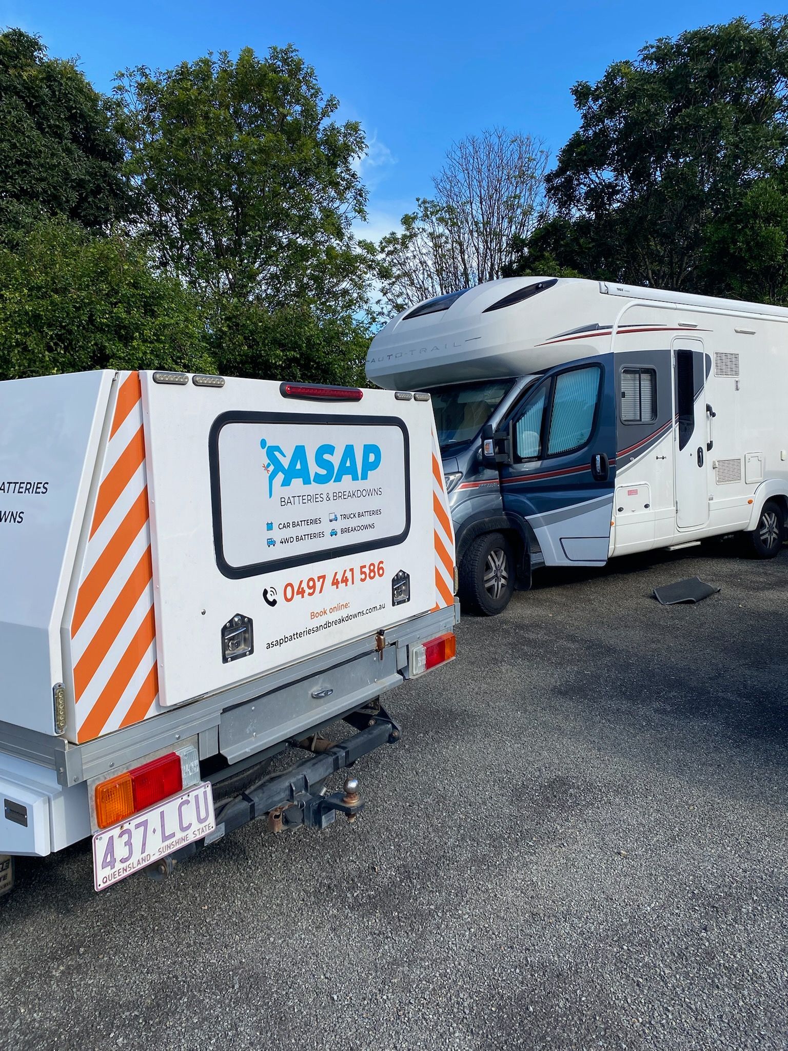 White camper trailer attached to a white utility trailer with orange stripes, near a parked RV against a tree line. — ASAP Batteries & Breakdowns in Burleigh Heads, QLD