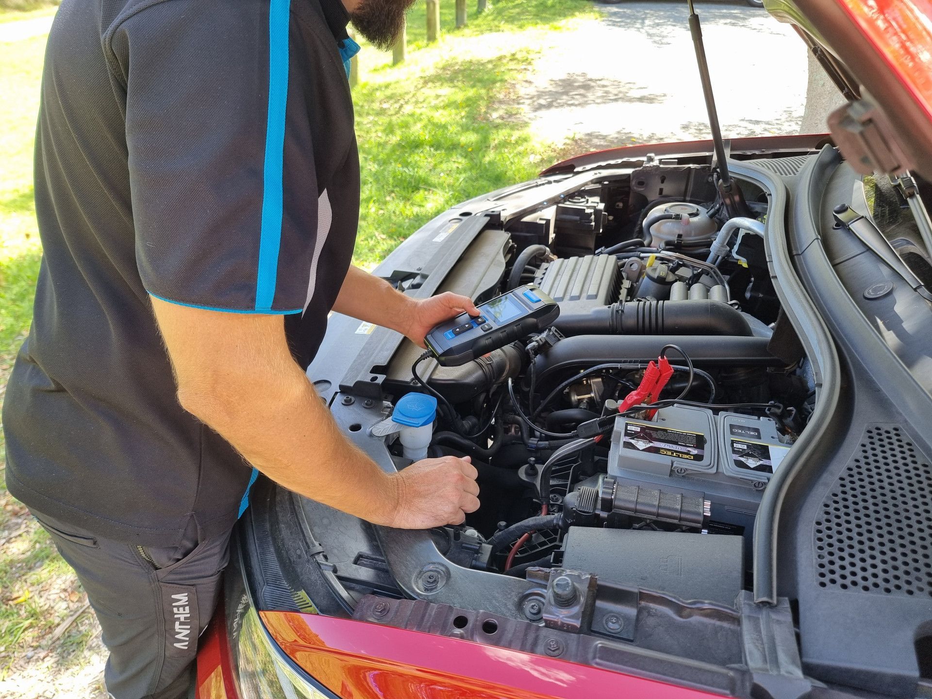 Mechanic using a diagnostic tool on a car engine. Red car, sunny outdoors. — ASAP Batteries & Breakdowns in Burleigh Heads, QLD