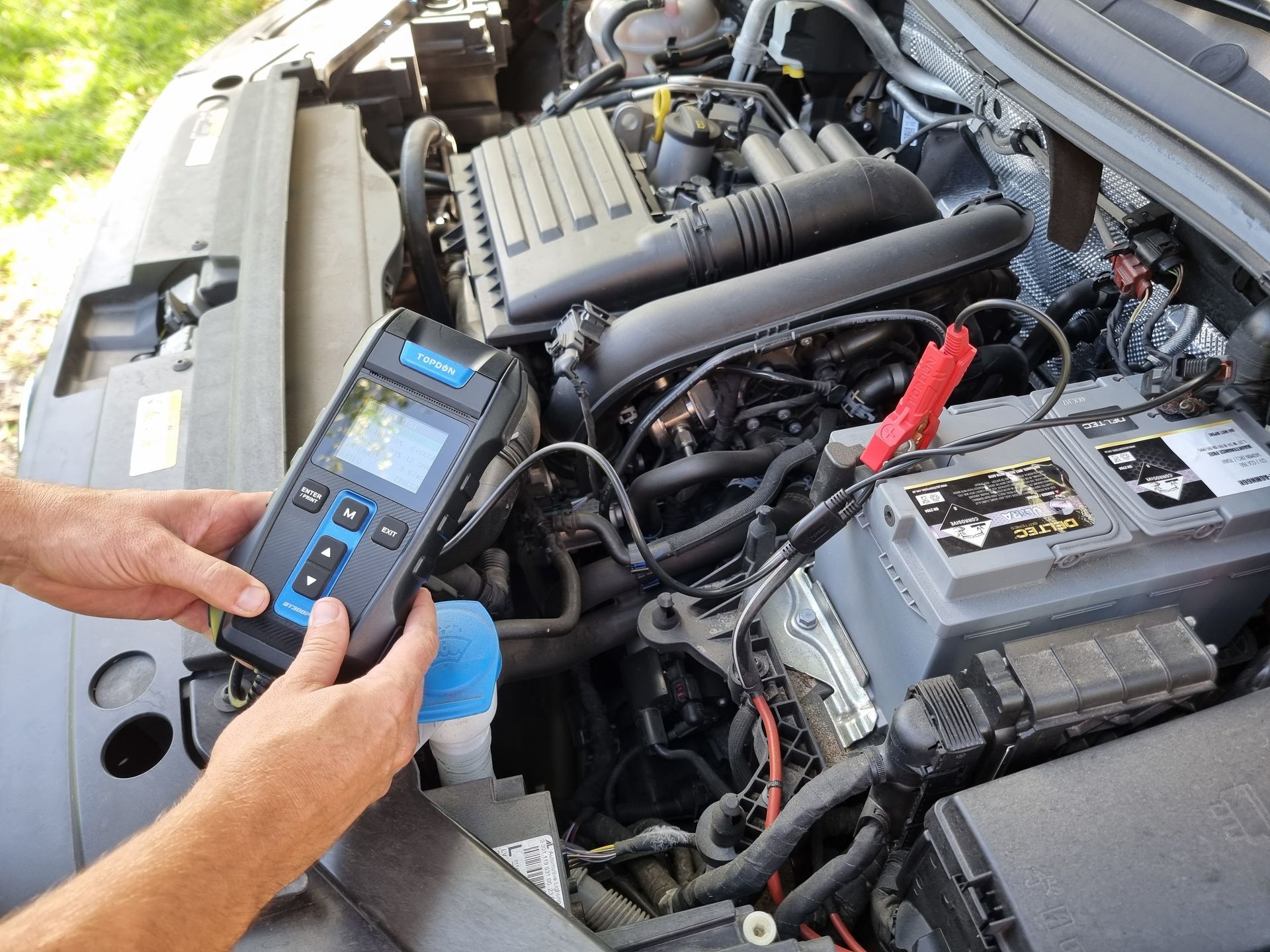 Person holding a battery tester connected to a car battery in an open engine bay — ASAP Batteries & Breakdowns in Burleigh Heads, QLD
