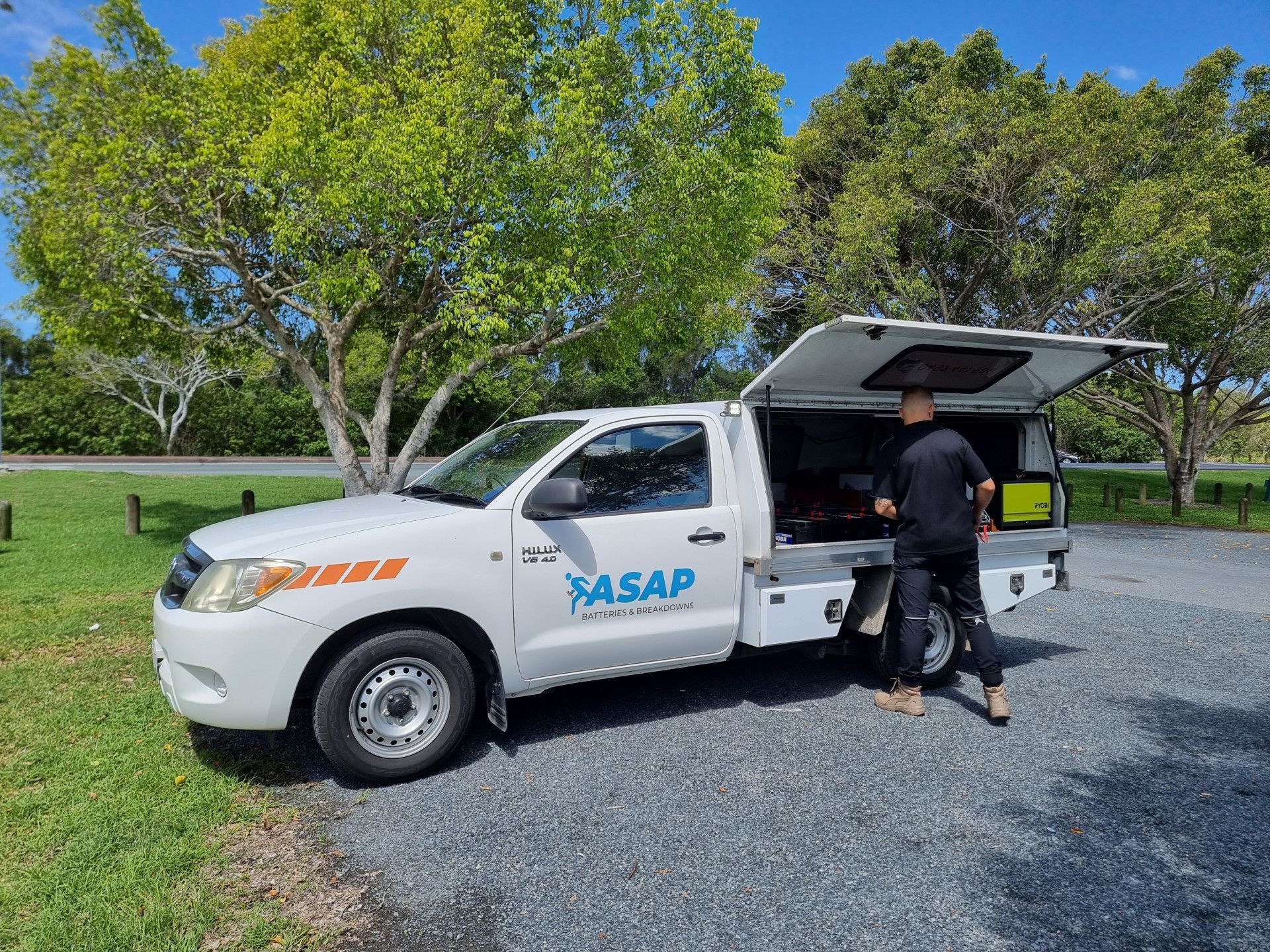 White service truck with ASAP logo, parked on gravel. A person is reaching inside the open back. Trees in the background. — ASAP Batteries & Breakdowns in Burleigh Heads, QLD