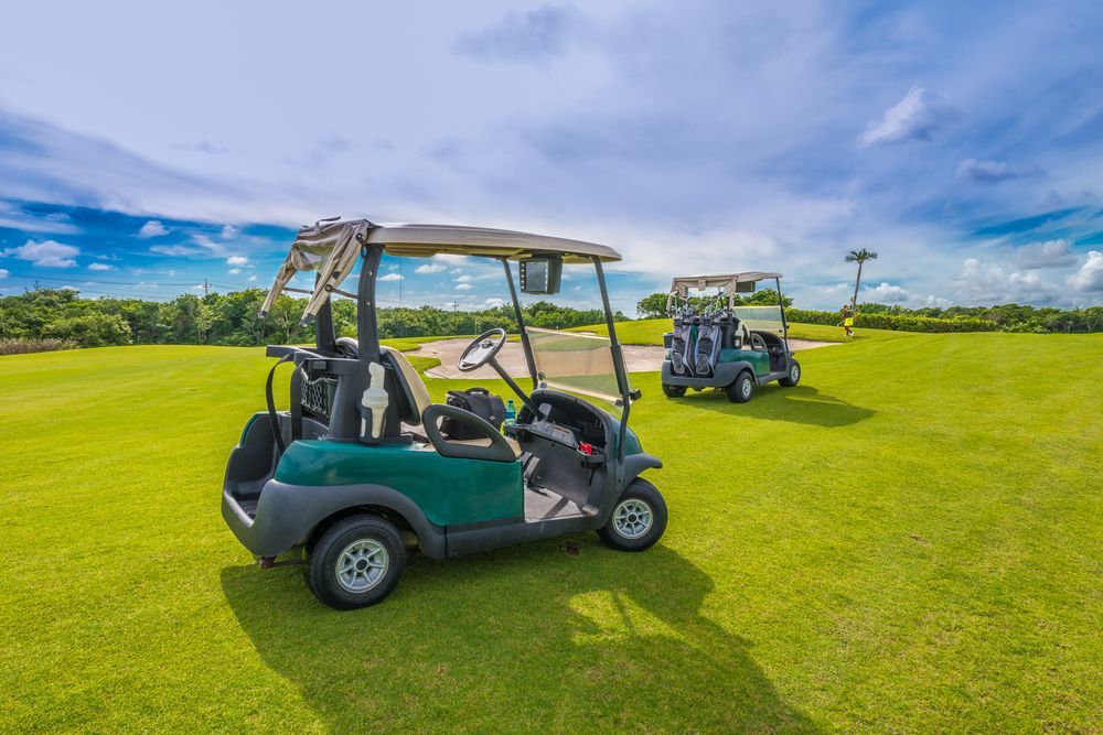 Two golf carts on green grass, one teal and one white, under a blue sky at a golf course. — ASAP Batteries & Breakdowns in Burleigh Heads, QLD