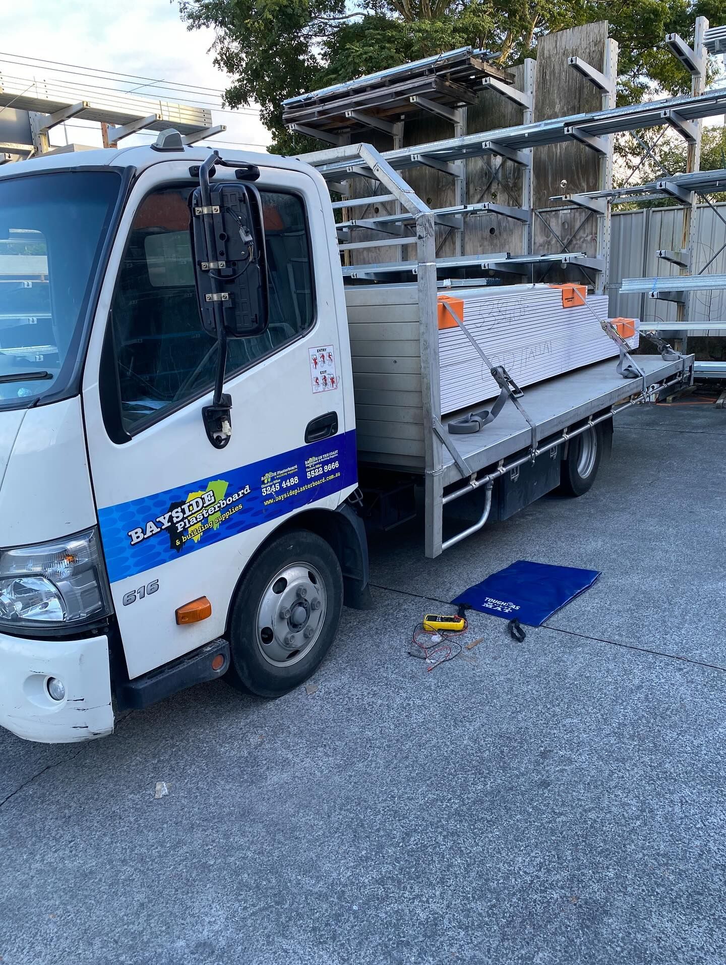 Work truck parked in an industrial yard, with tools and a battery tester laid out on the ground