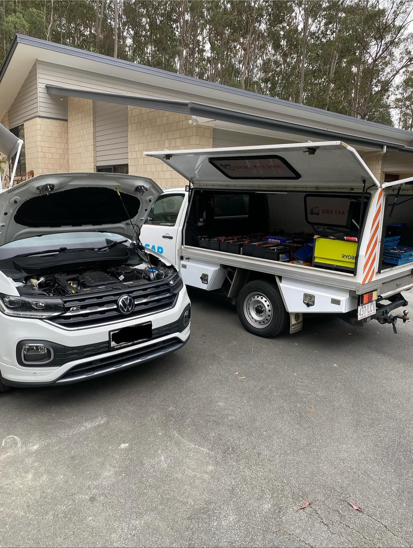 A white SUV with its hood up parked next to a white utility truck with an open canopy filled with tools on a driveway.