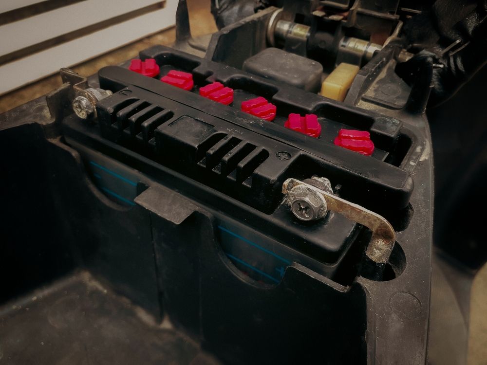 Black Motorcycle Battery in a Compartment, Secured With a Metal Clamp and Red Rubber Isolators — ASAP Batteries & Breakdowns in Burleigh Heads, QLD