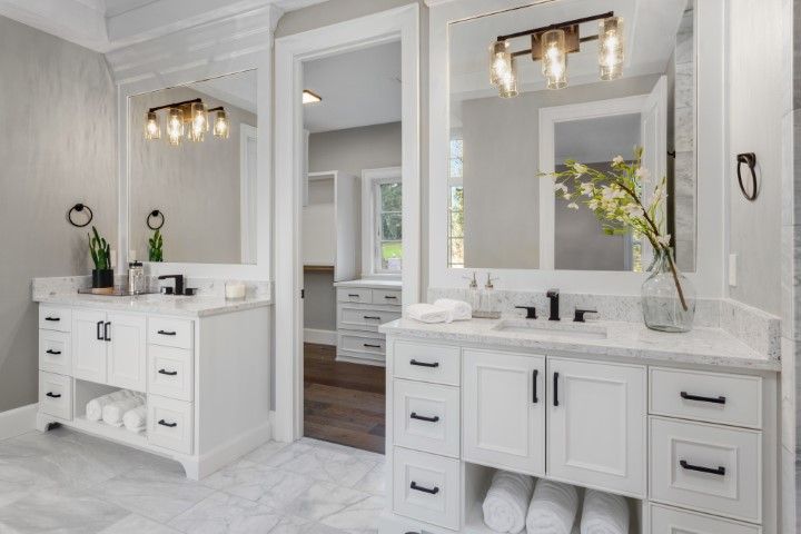 Two white bathroom vanities with mirrors, light fixtures, and black hardware.