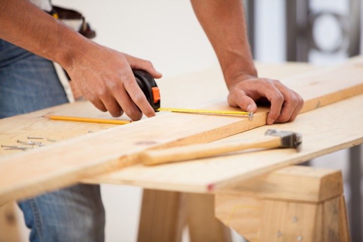 Carpenter measuring and marking wood with a tape measure and pencil on a workbench.
