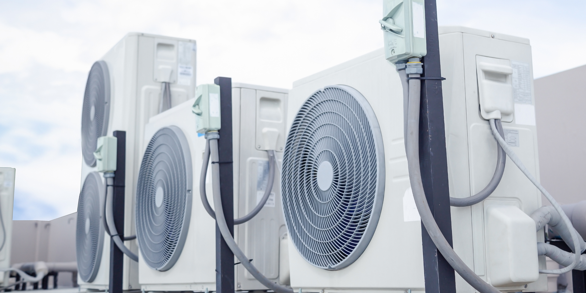 Outdoor row of white air conditioning units with large fans and connected hoses