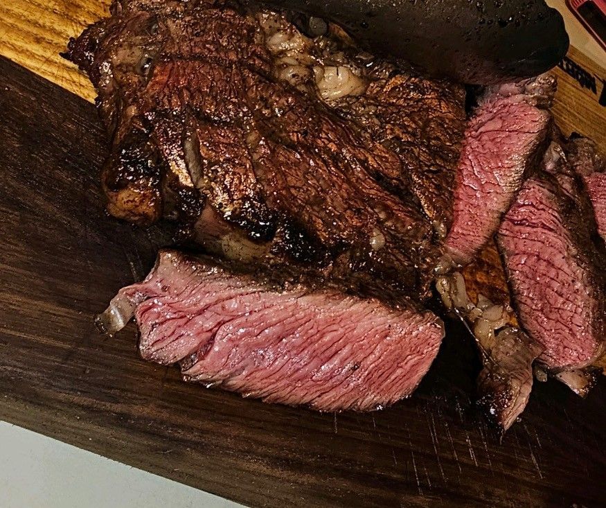 A piece of cut and grilled steak is sitting on a wooden cutting board.