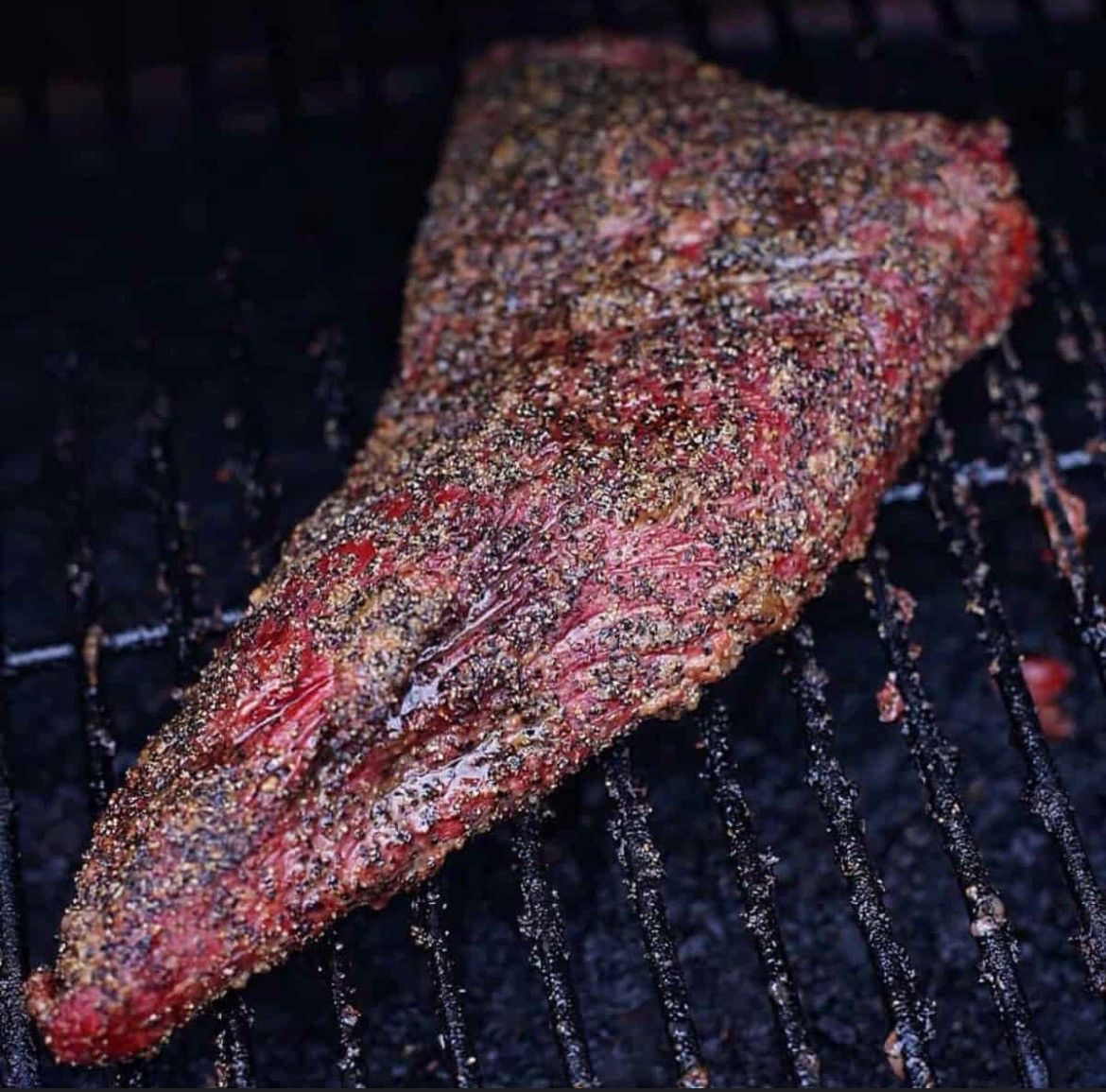A piece of meat is sitting on top of a grill covered in pepper.