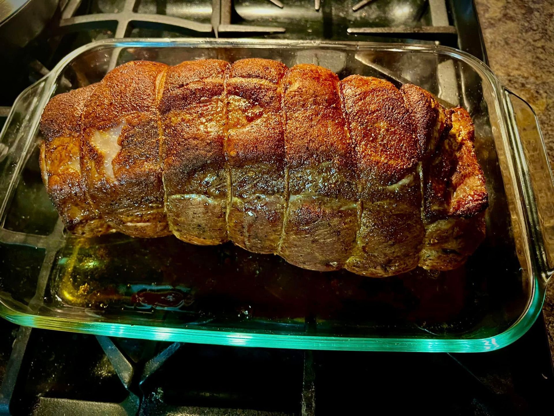 A large piece of meat is sitting in a glass pan on a stove.