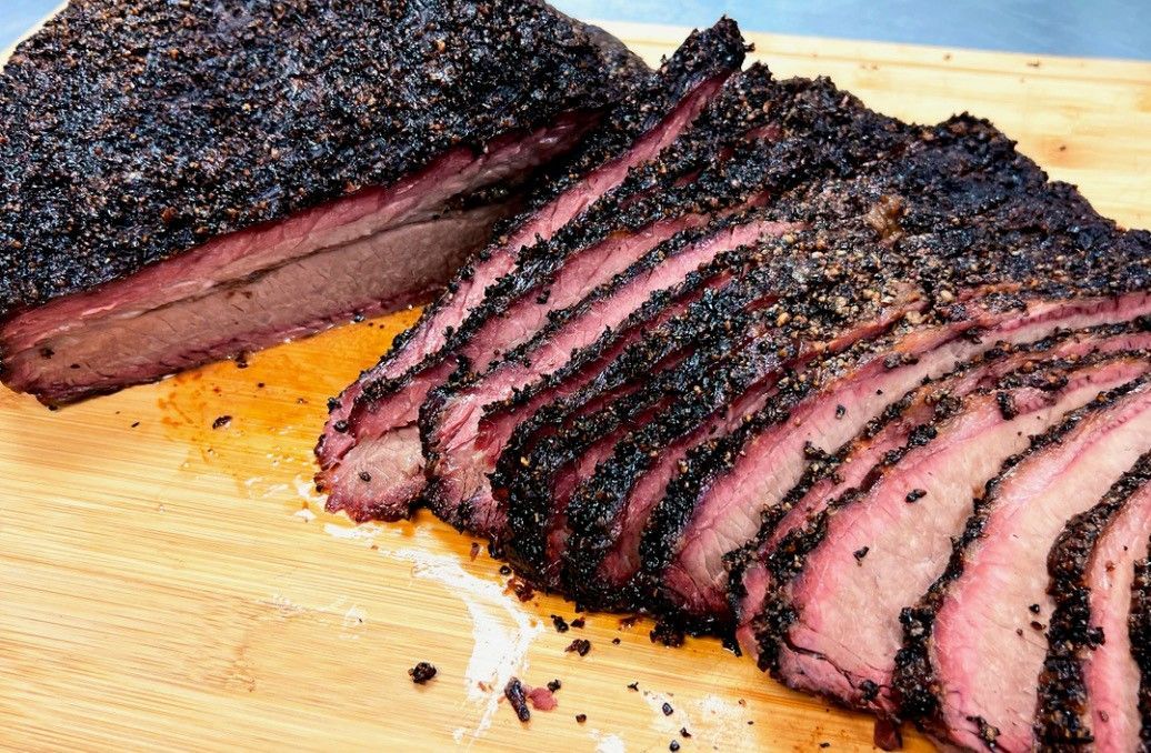 A large piece of smoked meat is sitting on top of a wooden cutting board.