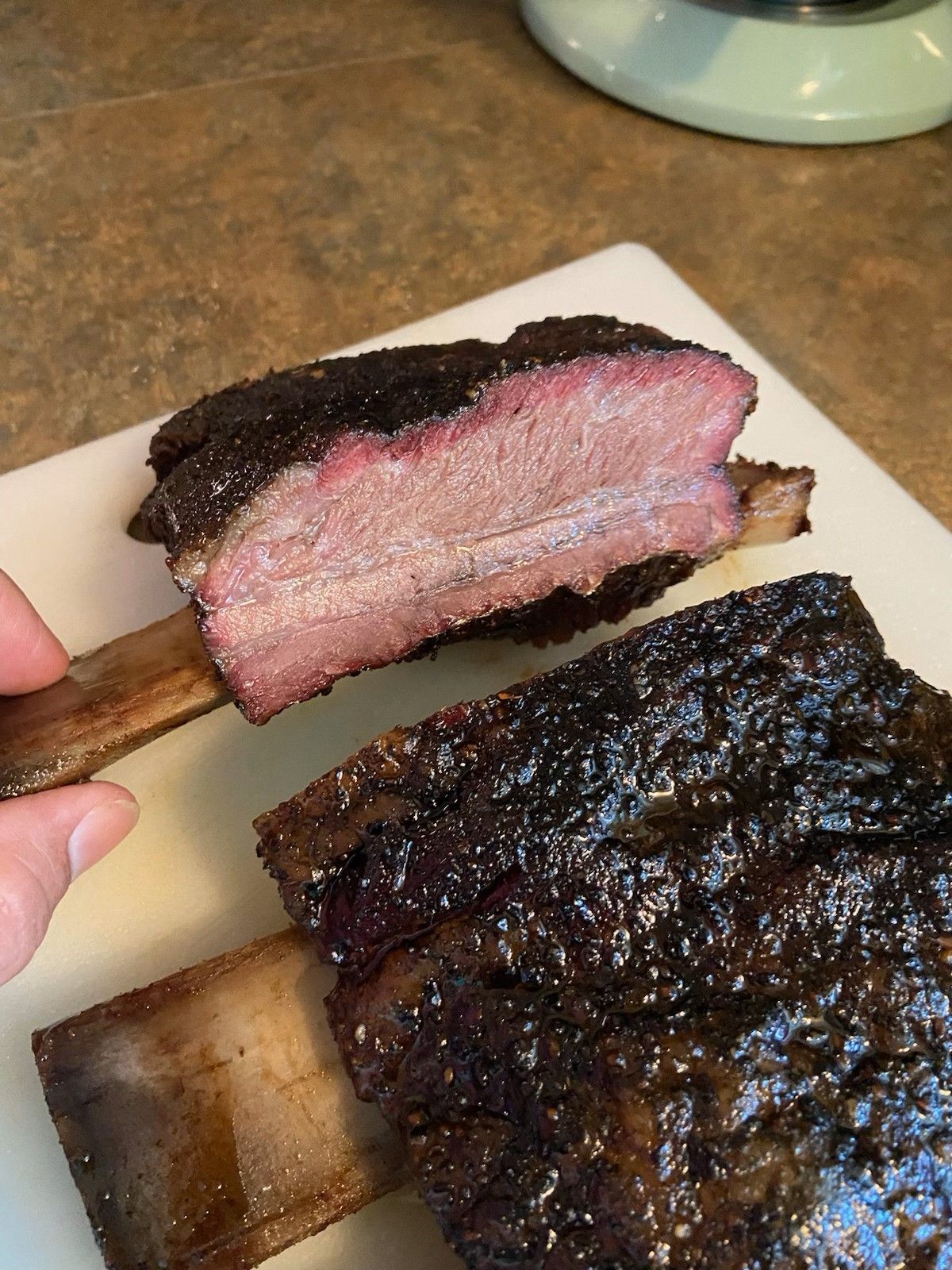 A person is holding a piece of in-house smoked meat on a cutting board.