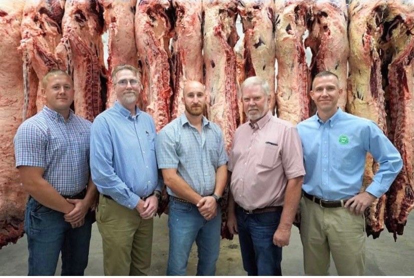 A group of men are standing in front of a wall of meat.