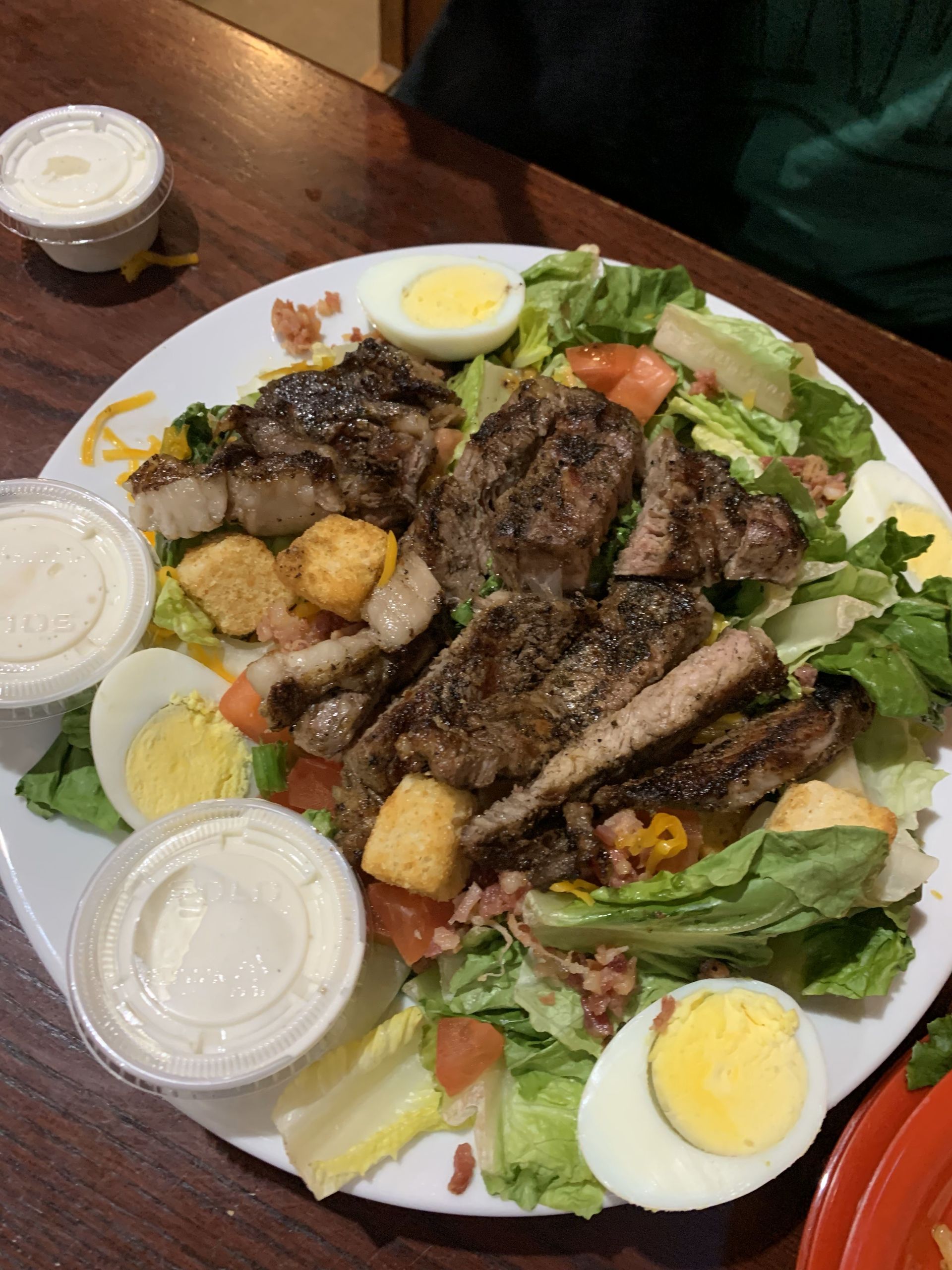 A salad with meat , eggs , lettuce and croutons on a plate on a table.