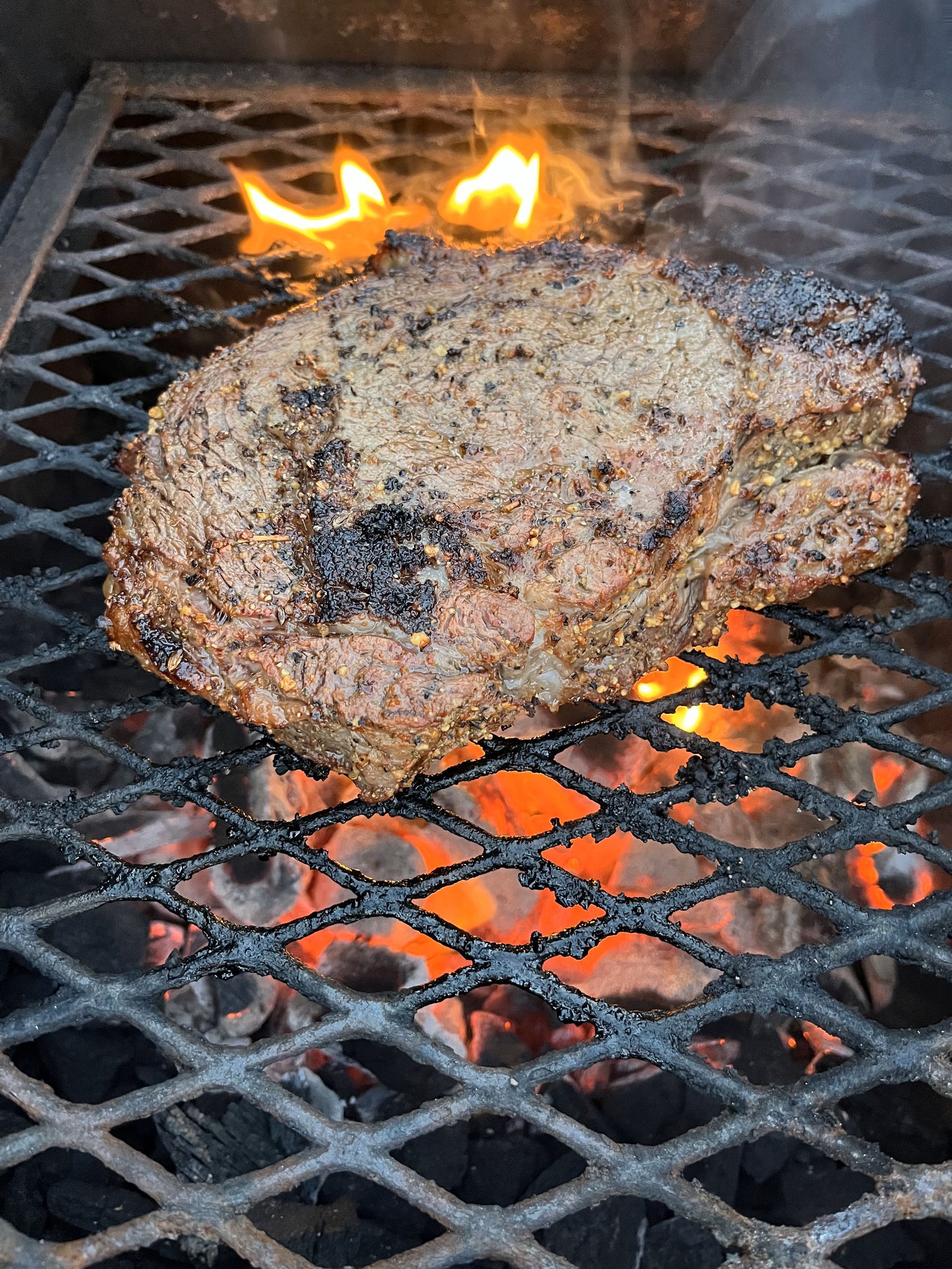 A large steak is cooking on a grill over a fire.