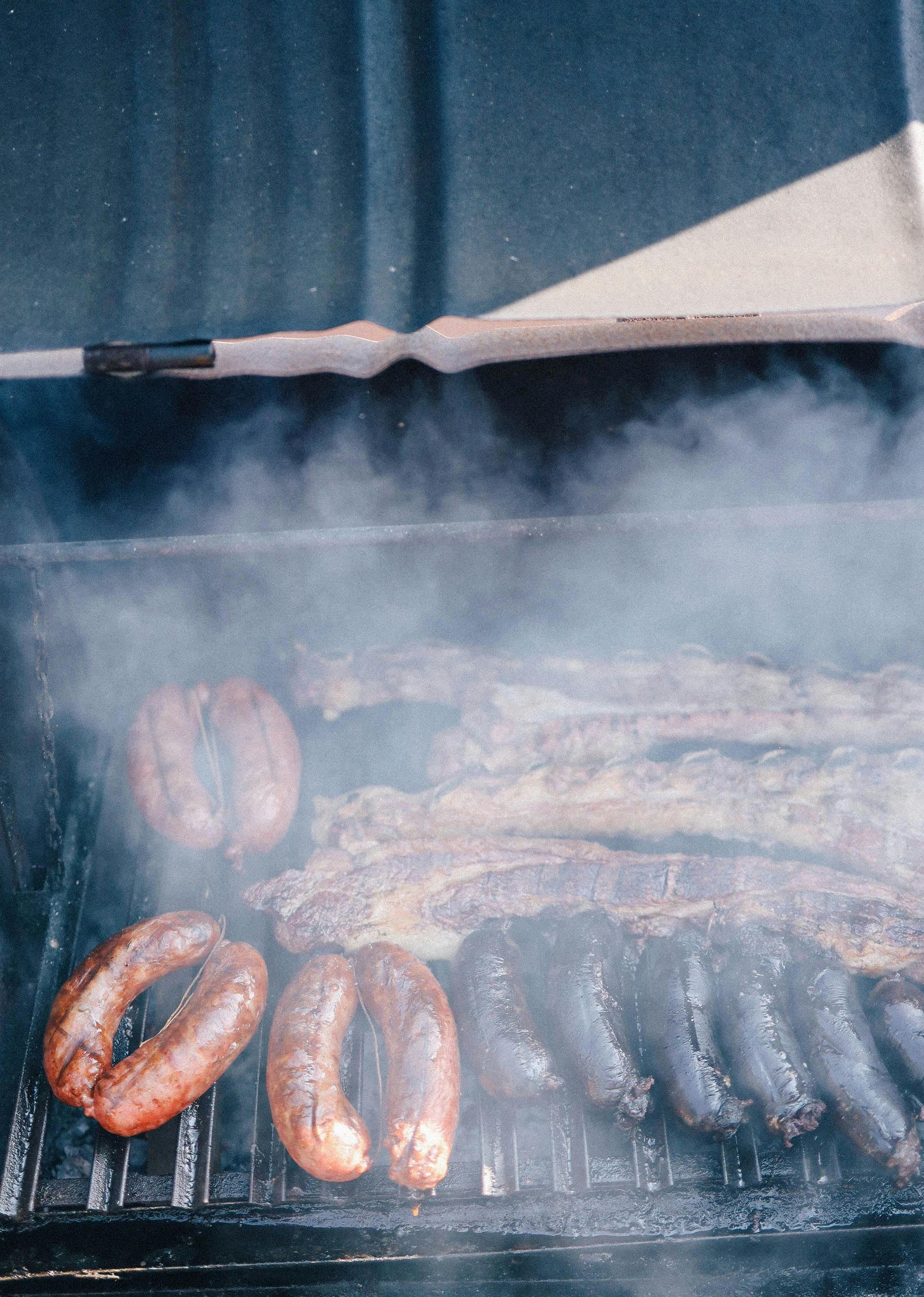 Sausages and meat are cooking on a grill with smoke coming out of it