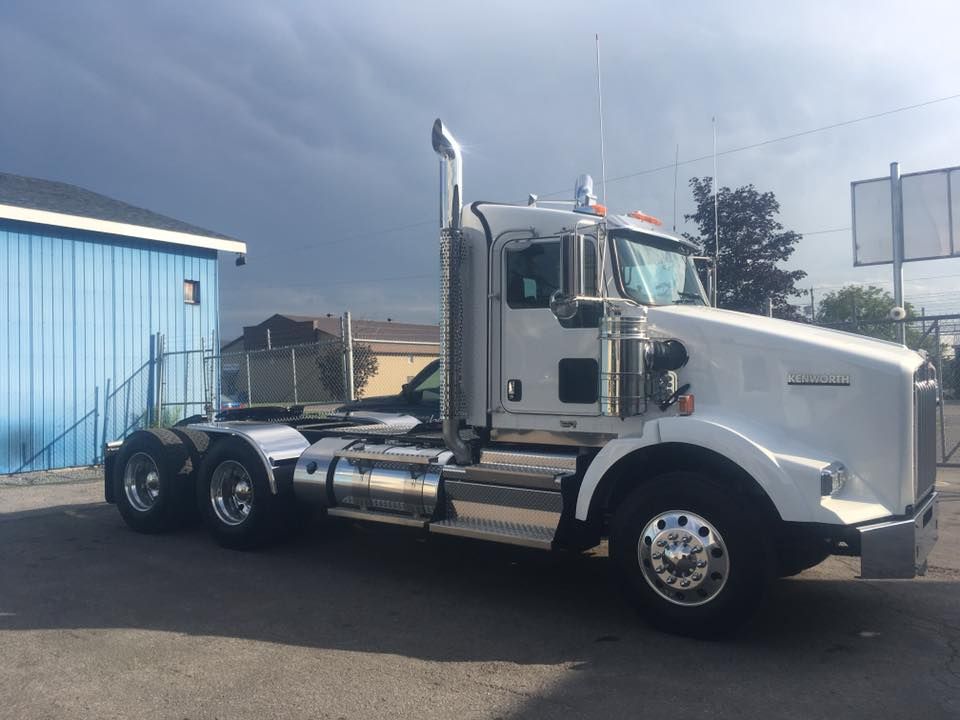 Un semi-remorque blanc est garé devant un bâtiment bleu.