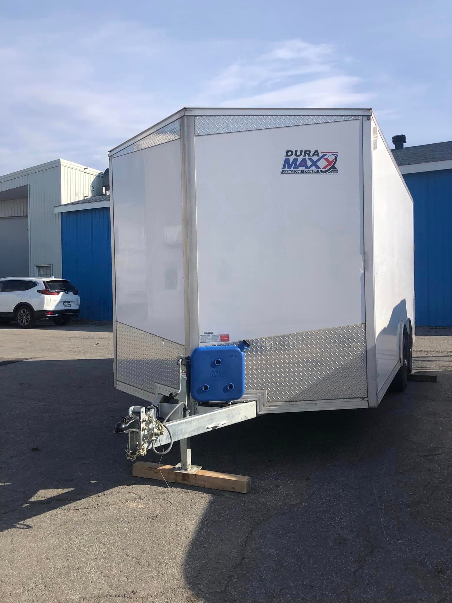 Une caravane blanche est garée dans un parking à côté d’un immeuble.