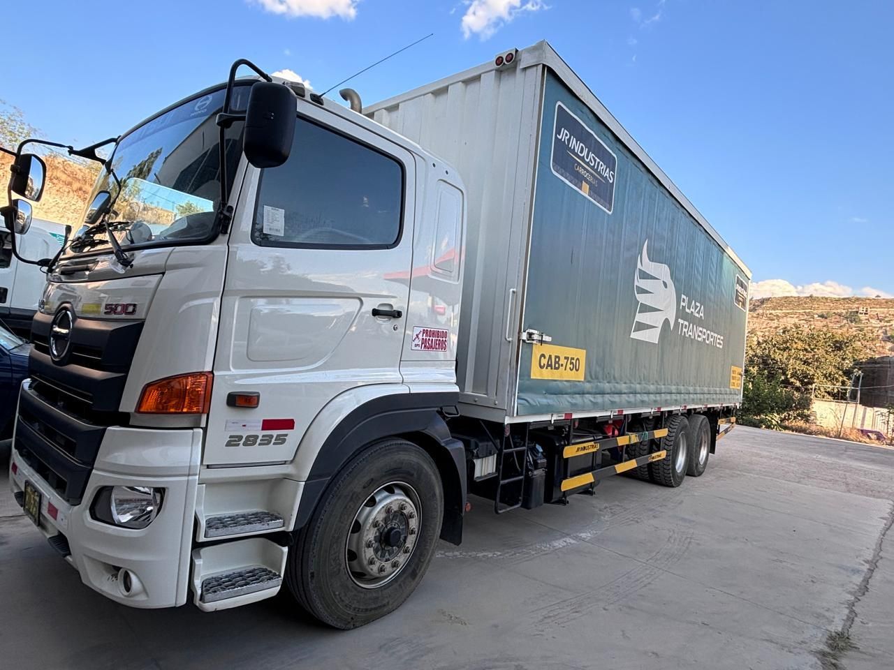 Camión Hino blanco con contenedor de carga cubierto, estacionado al aire libre en un día soleado.