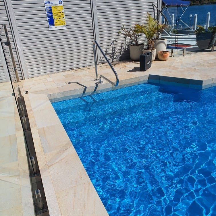 Swimming pool with blue water, steps, and a metal handrail. Beige tile surrounds the pool.