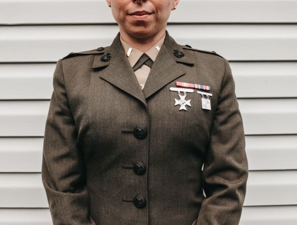 A service member in a green United States Marine Corps dress coat with ribbons and marksmanship badges.