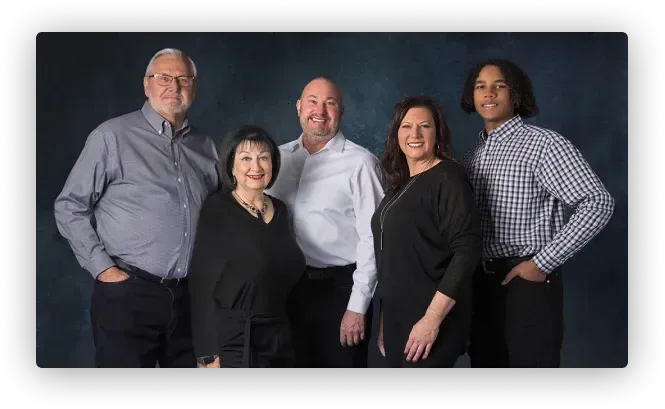 Five people stand together against a dark blue studio background, smiling for a professional portrait.