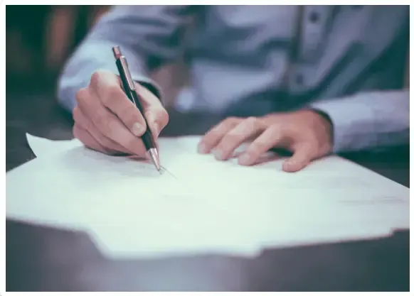 Close-up of a person’s hands using a pen to write on a white sheet of paper.