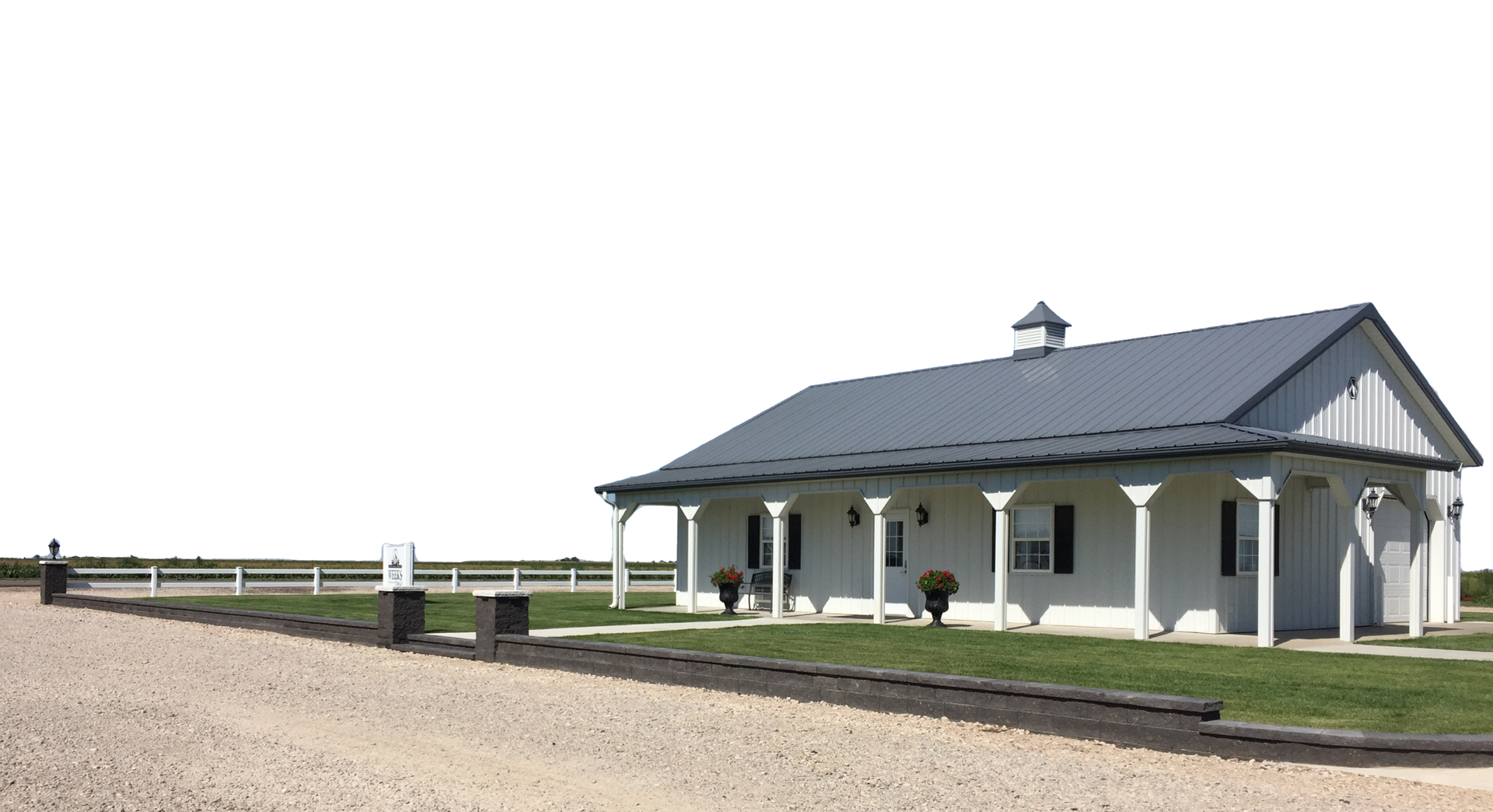 A white, one-story building with a dark roof and a covered front porch, situated in a field with a gravel driveway.