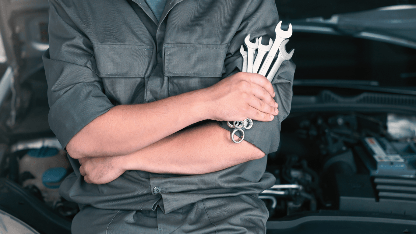 a mechanic leaning on a car holding wrenches