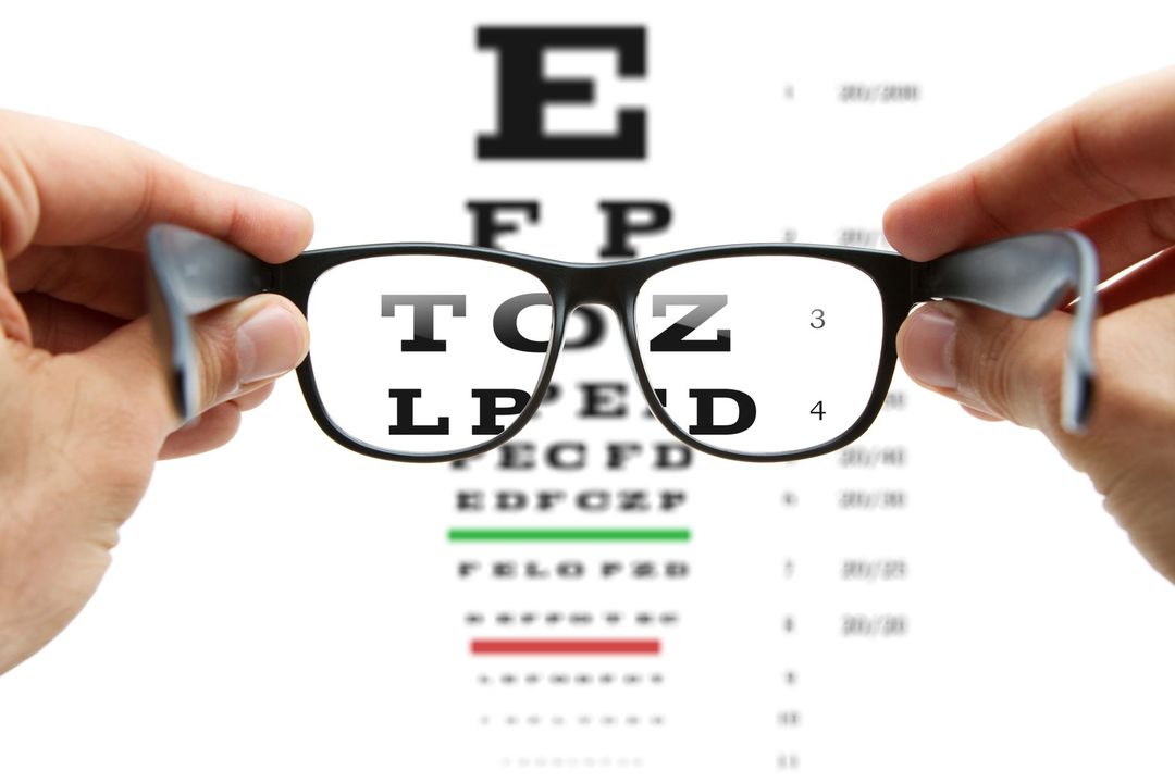 Mani che tengono gli occhiali davanti a una tabella oculistica, le lettere sono visibili attraverso le lenti.