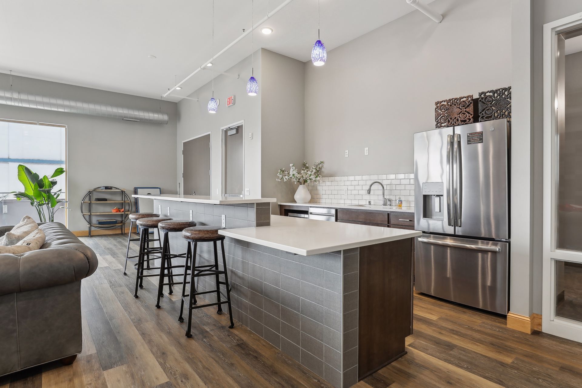 Open kitchen with island, stainless steel appliances, and seating. Wooden floors, gray walls, and pendant lights.