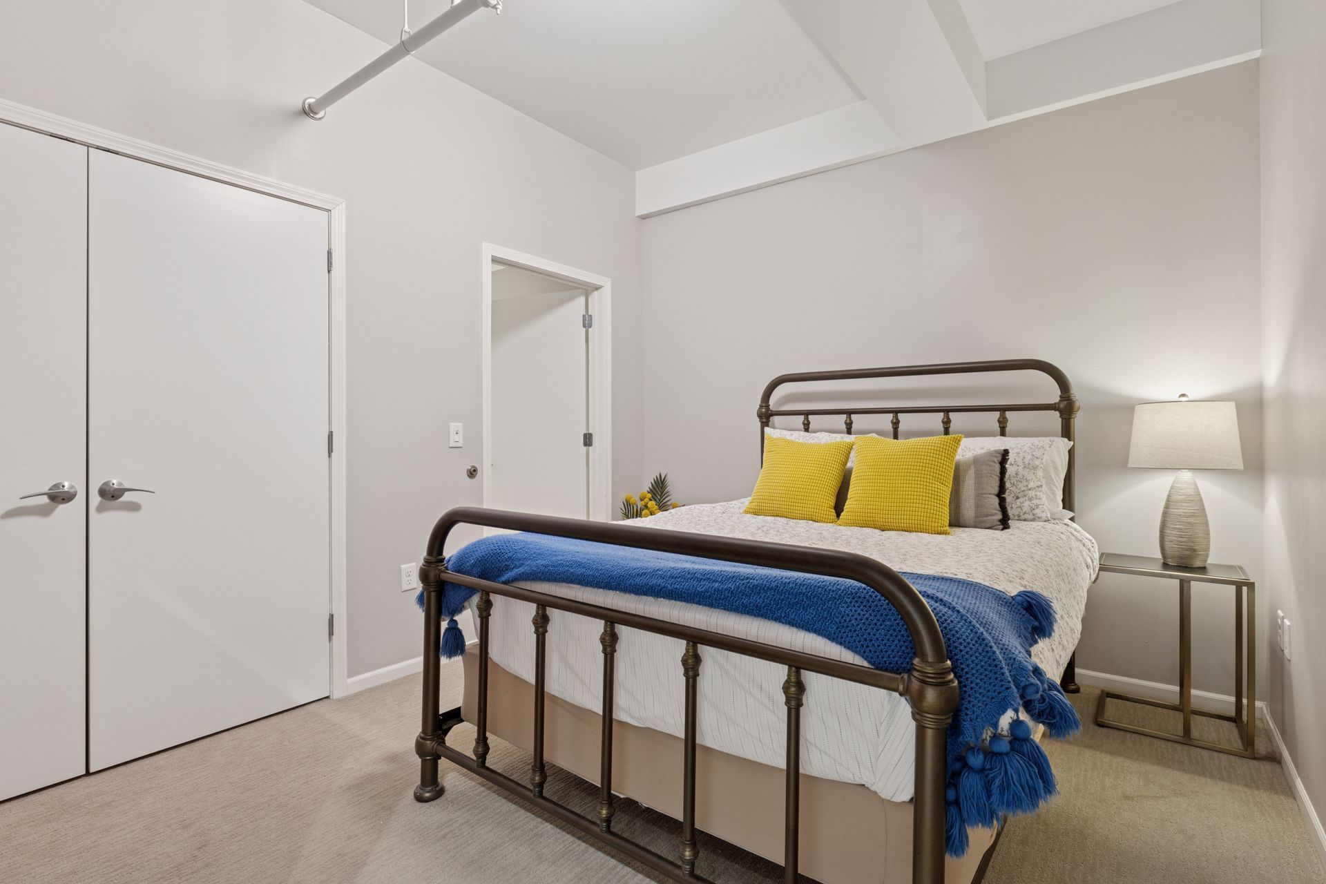 Bedroom with a bed, nightstand, and two white closet doors. Yellow and blue pillows and blanket.