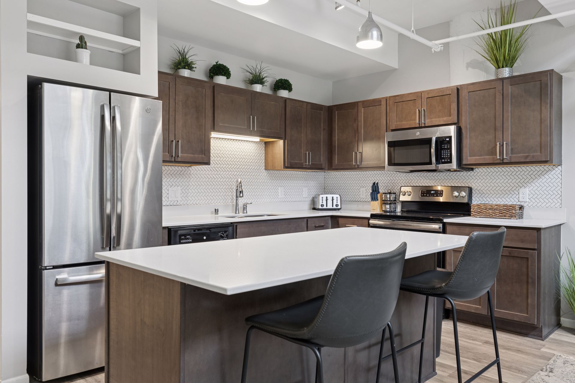 Modern kitchen with stainless steel appliances, dark wood cabinets, white countertops, and an island with two stools.