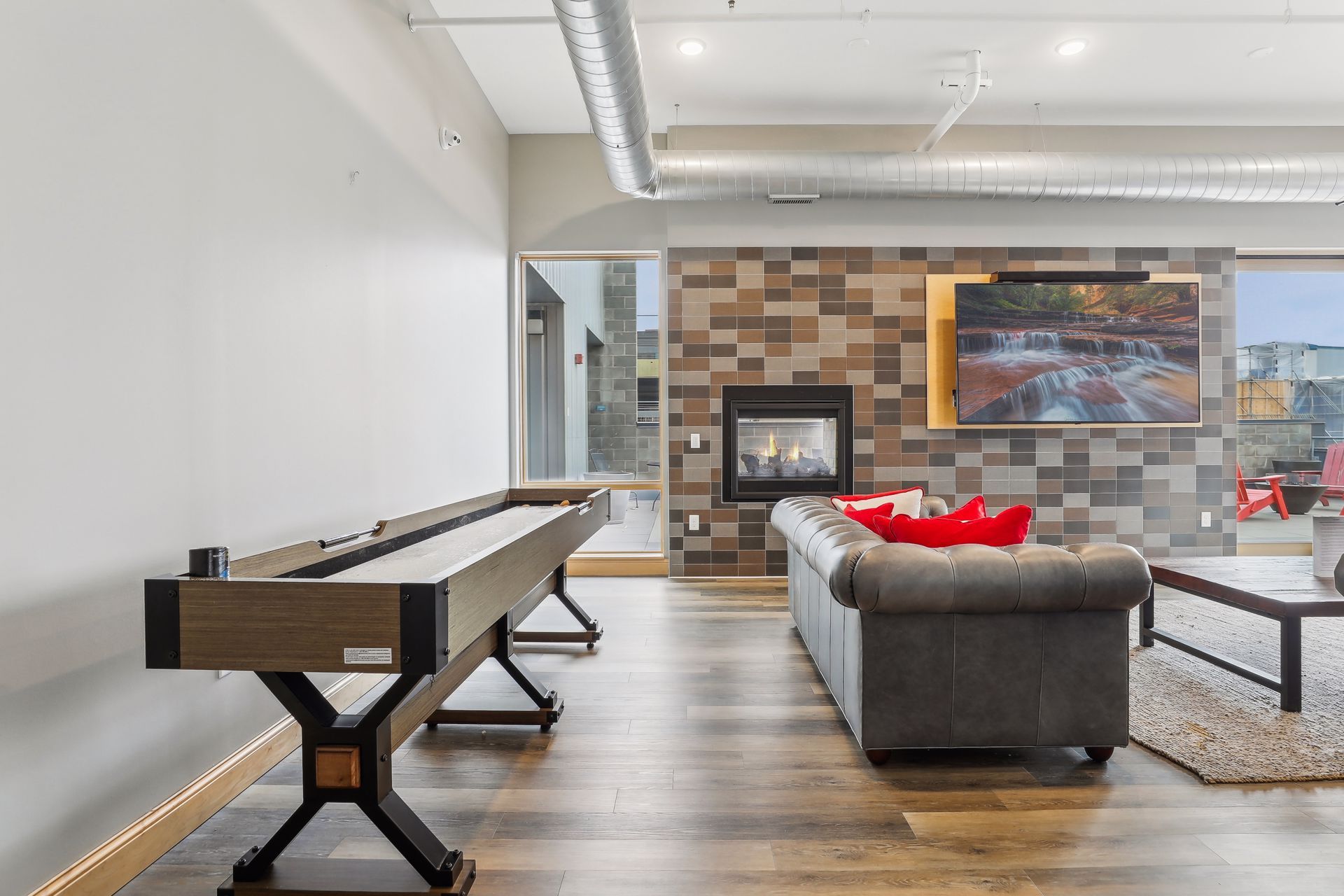 A modern living room with a shuffleboard table, fireplace, and gray couch.