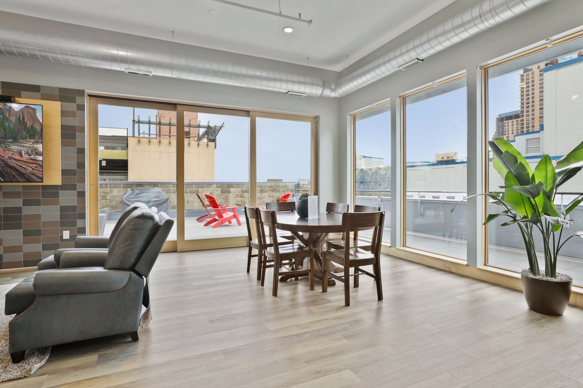 Living room with large windows, dining table, recliner, and a potted plant overlooking a rooftop patio.